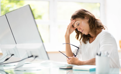 A woman at her desk visibly frustrated and rubbing her 